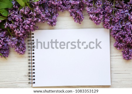 A bouquet of lilac flowers with notebook on a white wooden background. Copy space. Mothers Day. Top view.