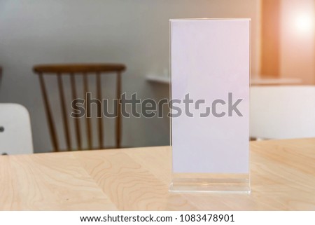 Stand mock up acrylic tent card menu frame on wood table in restaurant background.
Point of purchase advertising concept.
You can be used for message menu and  display products.