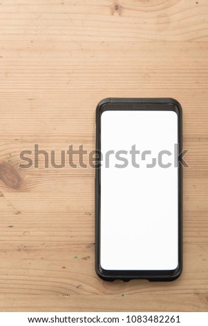 Mock up image of black mobile smartphone with blank white screen on vintage wood table background