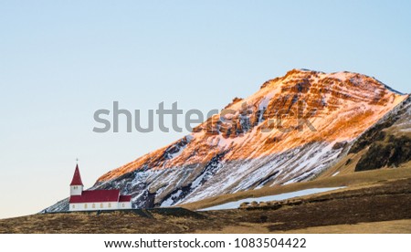 The Vik Church in Vik Village in Iceland. It is a famous and popular village for tourism. It is a red old lutheran church located on the hill and has a powerful mountain in background during sunset.