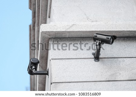 Two black security cameras watching the area near office building