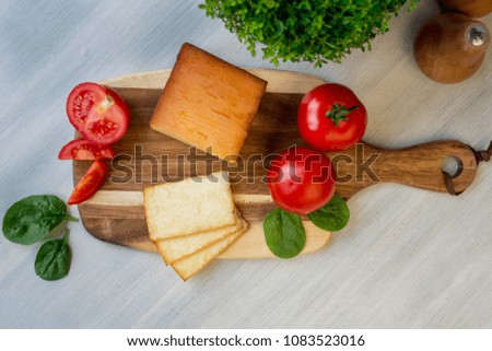 A block of smoked cheddar cheese and fresh tomatoes on wooden board