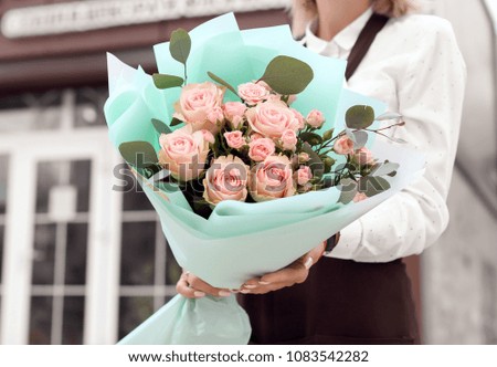 Female florist holding bouquet of beautiful flowers near shop