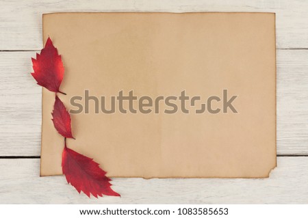 Three red leaves on blank worn paper on old worn weathered white wooden table