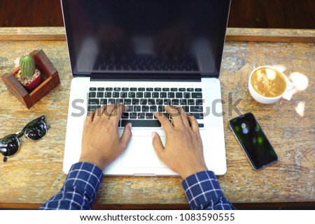 Top view A man hands typing keyboard laptop on wooden table with smartphone, coffee cup, sunglasses, cactus at coffee cafe. Working at home concept.       