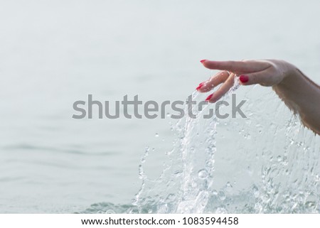 Female hands with red shiny nails in sea water and splashes