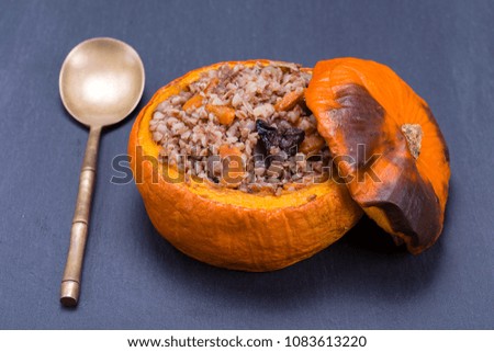 Tasty autumn stuffed pumpkin with buckwheat, carrot, onion, garlic and prunes on the background of black slate , close up