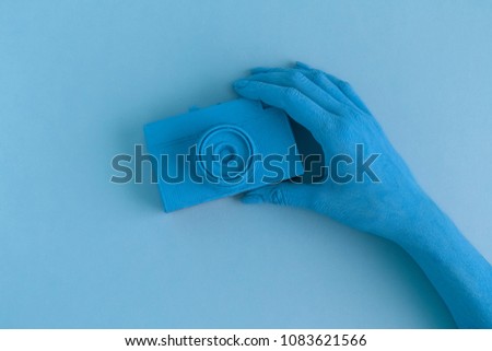 Female holding vintage film photo camera. Blue colored minimal abstract creative concept.