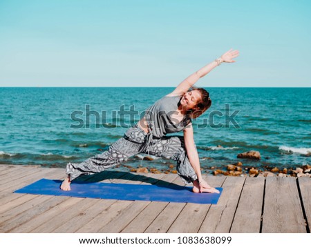 Young beautiful sporty woman in comfortable clothing doing yoga asana on sea beach near water. Girl practicing exercises. Health concept. Colorful picture.