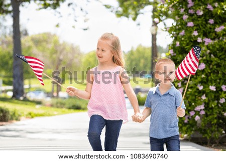 Young Sister and Brother Waving American Flags At The Park.