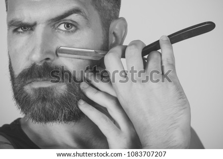 Fashion and beauty, innovation. Haircut of bearded man, archaism. Man cut beard and mustache with razor. Barber and hairdresser. Serious hipster in barbershop, new technology.