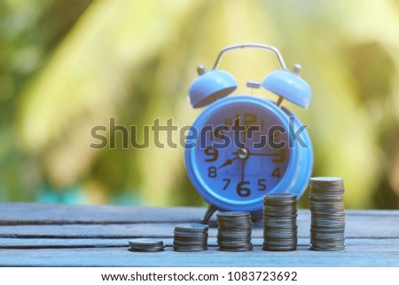 close up stack of coin and blue alarm clock on old wood table, nature copy space background for text, saving money for future, manage time for success business concept