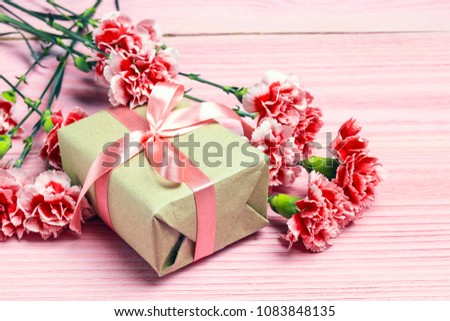 Gift box with carnations flowers on pink wooden background. Mother's Day background.