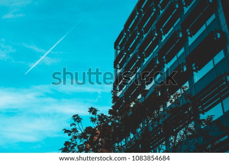 blue colored picture of office building with tree and airplane in the sky