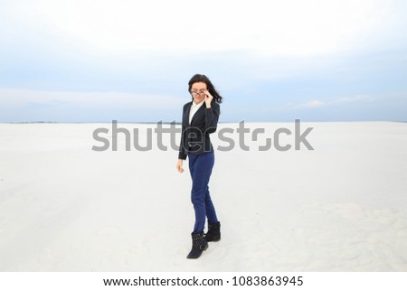 Young american businesswoman standing on snow in monophonic background, wearing glasses and jacket. Concept of wintere seasonal photo session and business.