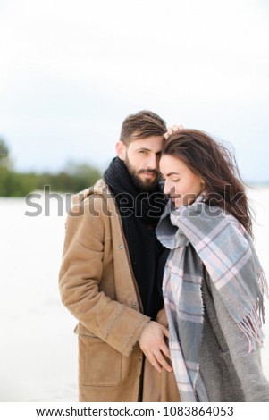 Young nice woman wearing grey scarf standing with man in coat, winter white background. Concept of couple photo session, seasonal inspiration.