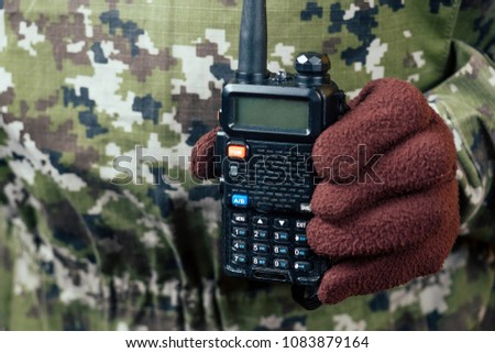 the man in the camouflage and gloves is holding the walkie-talkie in his hand