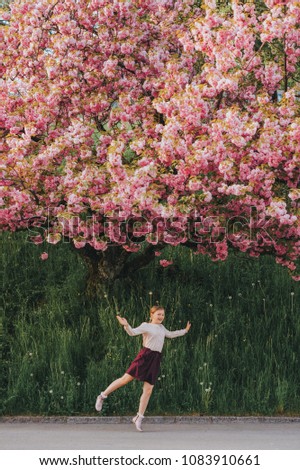 Spring image of blooming sakura. Kid girl playing with decorative cherry tree, happy childhood in countryside