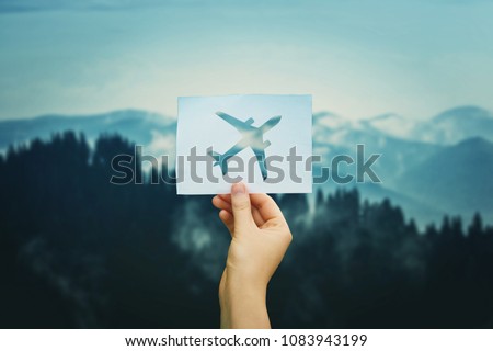 Hand holds a paper with plane icon over silent nature background. Love travel concept. Flight restrictions due coronavirus COVID-19 pandemic outbreak. Only charter flight allowed. Quarantine concept. Royalty-Free Stock Photo #1083943199