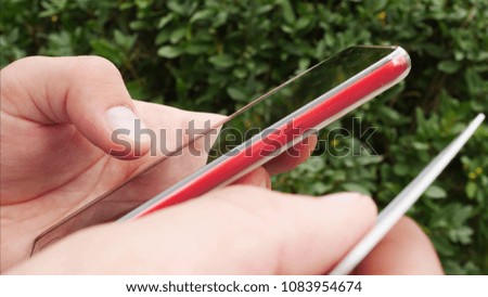 Man hands holding red smartphone and debit or credit card and buy online outside in park on background of green bushes