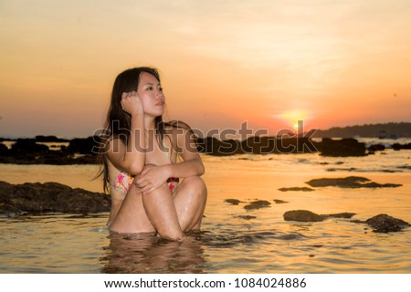 young beautiful and attractive Asian Korean woman relaxed enjoying water and rocky landscape at beach sunset under orange sky in Summer holidays travel and Asia trip destination concept 