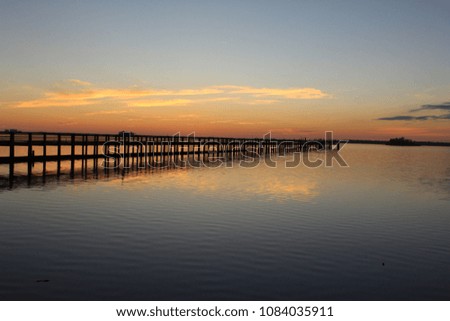 Beautiful sunset sky with water reflection by a wooden fishing pier jetty