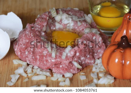 minced meat and raw egg and chopped onion next to the shell and jars of pepper and salt