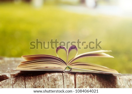 Book on a wooden table in garden with pages forming heart shape. 