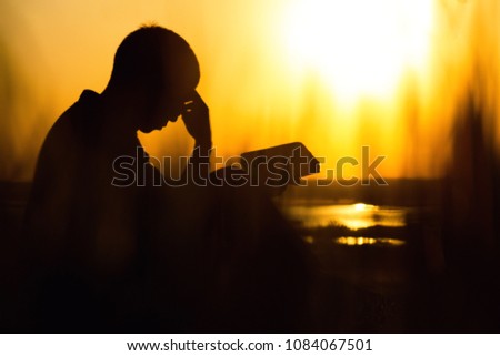 silhouette of a young man with a Bible in his hands in the field, male praying to God iwith remorse and gratitude in nature, faith in difficulties of life, the concept of religion and spirituality Royalty-Free Stock Photo #1084067501