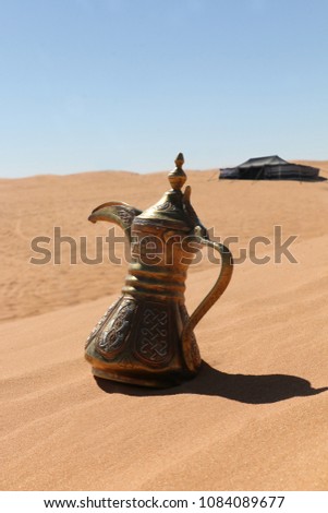 A traditional middle eastern pot called  dallah on a red sand dune desert with a bedouin tent at the background