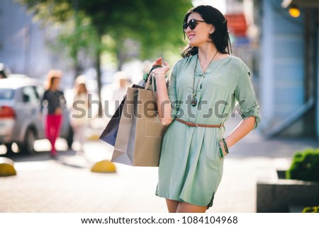 woman in glasses and tunic with a belt goes in the street in the city with packages in her hands Royalty-Free Stock Photo #1084104968