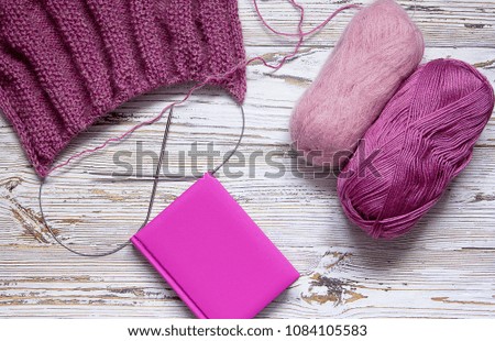 Yarn for knitting, knitting needles and a sweater on a white wooden vintage background. Pink yarn and handmade scarf on an aged background.