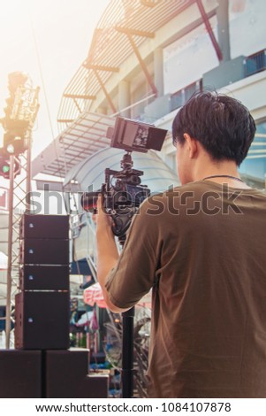 Back view of a single young man cameraman shooting the film scene with camera on street. DSLR camera for video production are shooting movie. Videographer by event.