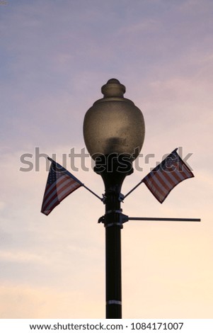 Old fashioned lamp post with American flags waving with a subtle Midwest sunset in background.  Peru, Illinois, USA