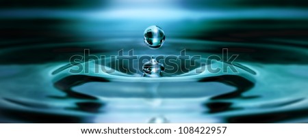 Single water drop bounces back from the water surface floating in the air and creating a nice wave in the water. Royalty-Free Stock Photo #108422957