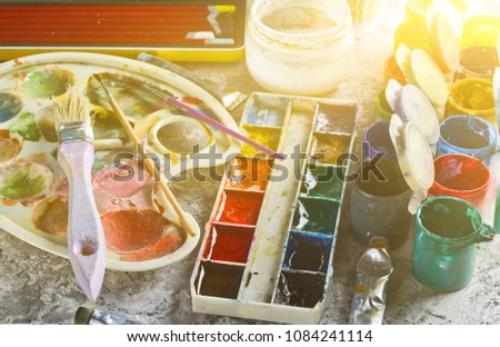 Artistic tools for drawing paintings on a gray concrete background. Palette, gouache, oil paint, brushes, colored crayons, pastel, colored pencils. 
