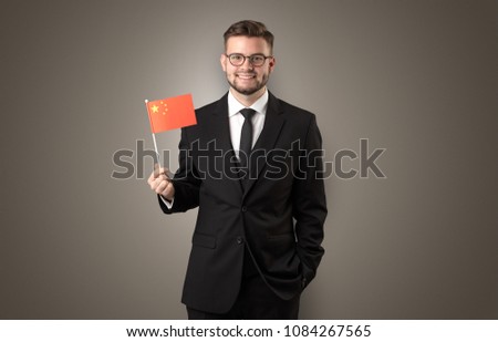 Cheerful student standing in front of wall with national flag on his hand