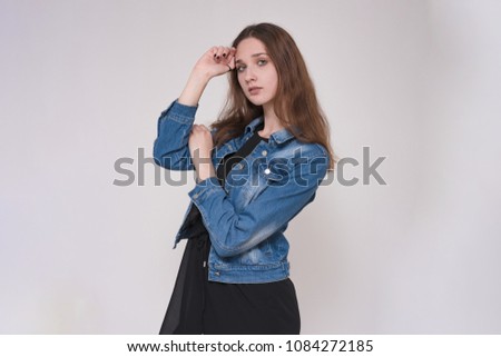 I listen carefully to you. Portrait of a beautiful brunette girl on a gray background in a denim jacket. She is standing right in front of the camera and looks happy
