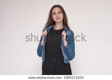 I listen carefully to you. Portrait of a beautiful brunette girl on a gray background in a denim jacket. She is standing right in front of the camera and looks happy