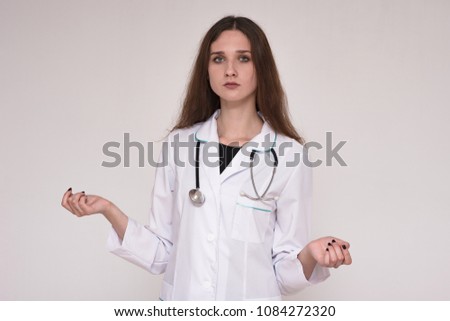 I am a doctor and I listen to you carefully. Portrait of a female student doctor on a gray background in a white coat. She's standing right in front of the camera and looks serious.