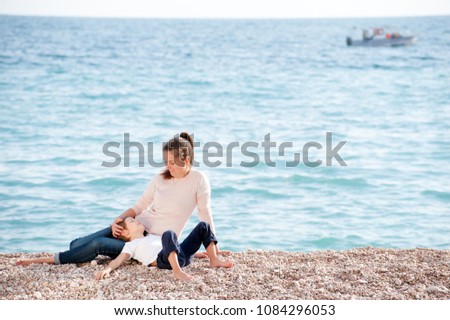 happy family consisting of mother and little kid resting on ocean beach in early summer day