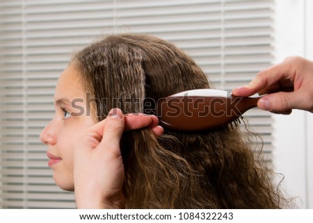 girl with curly hair, sitting at the stylist combing hair comb.