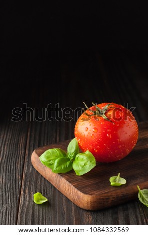 Red tomato on a cutting board with basil leaves on wooden background. Copy space. Fresh tomato wased for cooking. Tomato with droplets of water, Royalty-Free Stock Photo #1084332569
