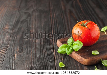 Red tomato on a cutting board with basil leaves on wooden background. Copy space. Fresh tomato wased for cooking. Tomato with droplets of water, Royalty-Free Stock Photo #1084332572