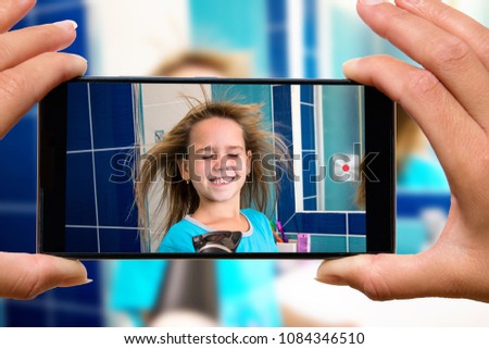 Woman with mobile phone photos child in the bathroom.