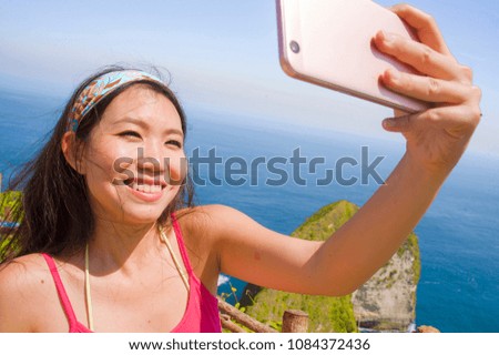 young beautiful and happy Asian Korean tourist woman smiling taking selfie portrait with mobile phone in beach sea cliff landscape background in internet travel blog and hollidays destination concept