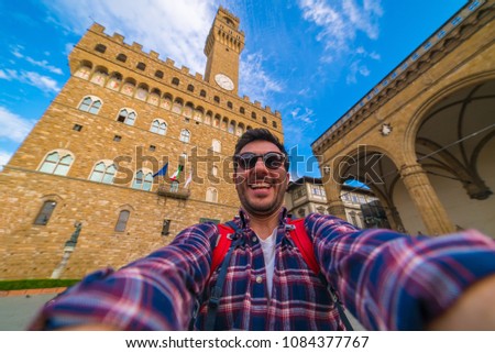 Tourism in Florence. Happy tourist man take selfie photo in front of The Old Palace (Palazzo Vecchio or Palazzo della Signoria) in Florence, Tuscany, Italy