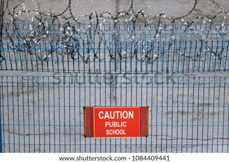Iron fence with barbed wire. Metallic fence with red warning sign Public school.