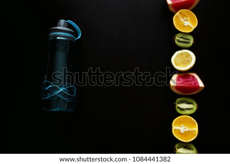 Fitness bottle of water and different fruits on black table. Background layout with free text space.