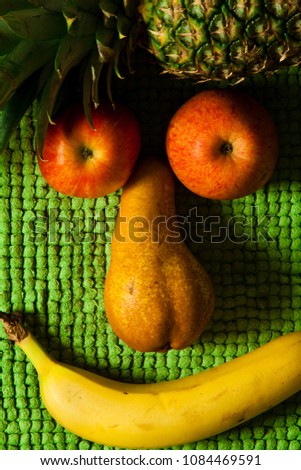 Face fruit smile. Apple, pear, pineapple and banana. Plush green background. The fruit is positioned to form a sympathetic human face smiling.